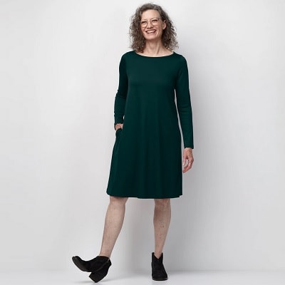 A white woman with long curly hair wearing a green dress with black ankle boots