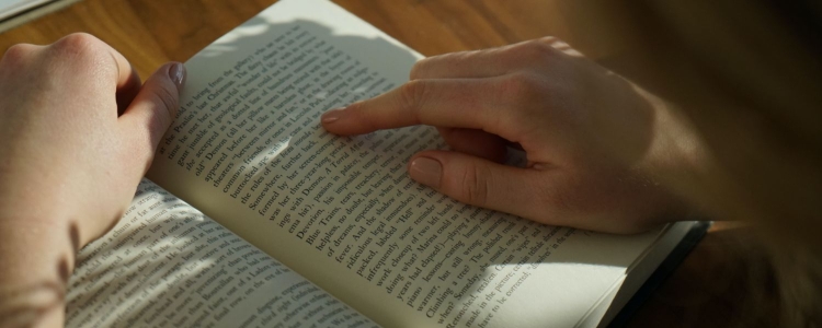 young woman reading a book, her finger pointing at words