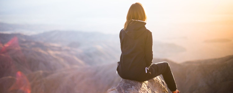 woman siting on mountain peak overlooking a beautiful vista