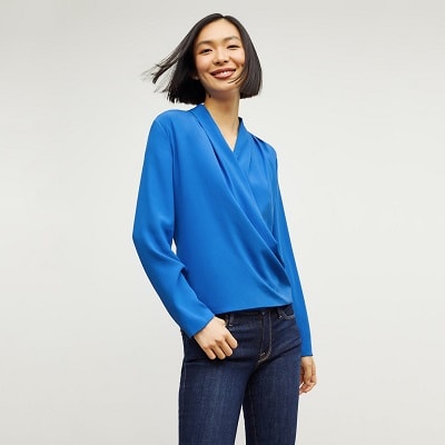 A woman with a short black bob wearing a blue wrap top and dark blue jeans 