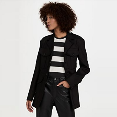 A Black woman with short natural hair wearing a black blazer, black-and-white striped top, and black pants (legs cropped out)