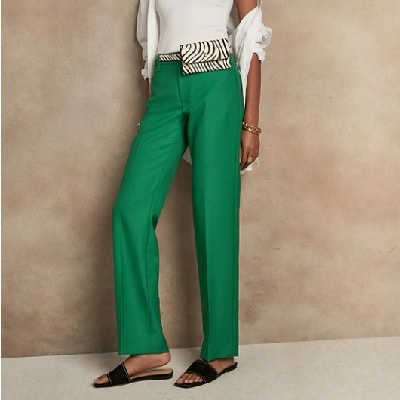 A woman wearing green tailored pants, black sandals, and a white shirt (upper body cropped out)