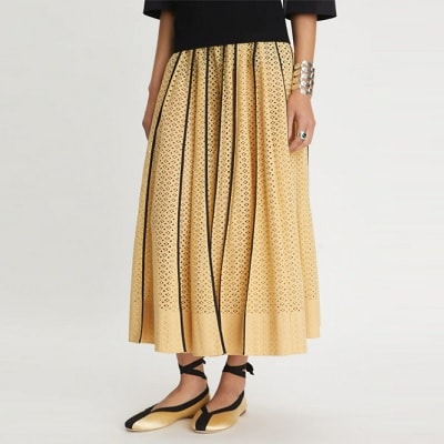 A woman wearing a yellow eyelet skirt with black vertical stripes, along with silver jewelry and yellow-and-black flats (upper body  cropped out) 