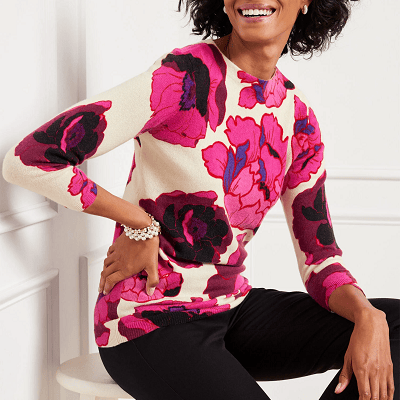 professional woman models cashmere sweater with crew neck; it has a bright pink floral print against an ivory background