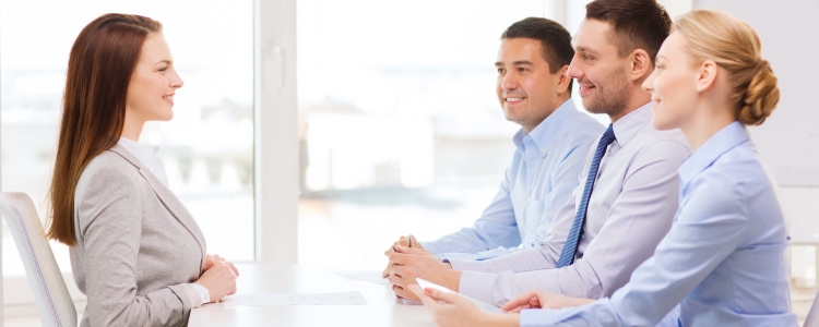 professional woman in a blazer interviewing with a team of men and women wearing blue button-front shirts