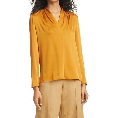 A woman with long curly black hair wearing a mustard-colored silk blouse and loose tan pants