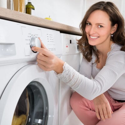 young professional woman smiles as she puts washable pants in the washer and dryer
