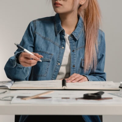 woman with pink and blonde hair works at a desk; she is wearing a blue denim jacket and white t-shirt