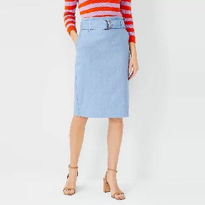 A woman wearing a pink-and-red striped top with a blue chambray skirt and tan sandals