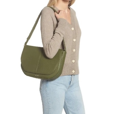 blonde model with blue jeans and a beige sweater has an olive green purse over her shoulder