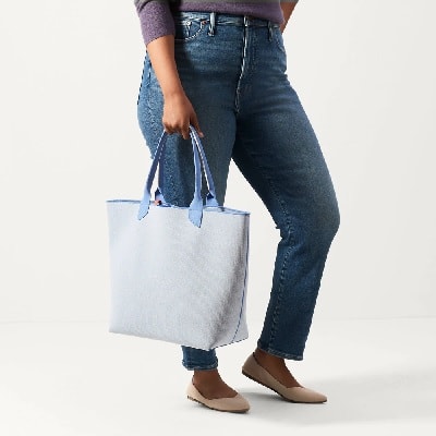 mid-size model in blue jeans holds a light blue tote