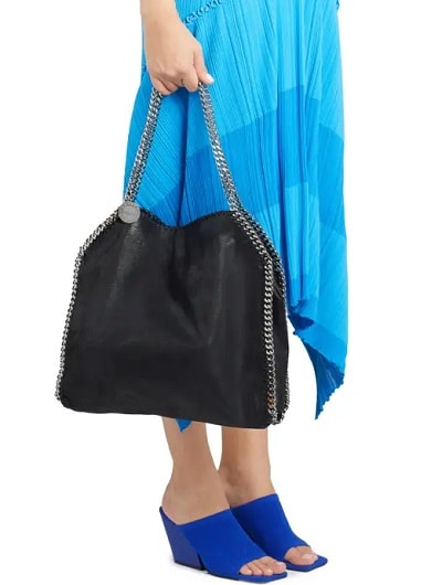 woman wearing a blue dress holds a black tote with chain straps