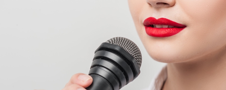 woman with bright red lipstick and a white blouse speaks into a microphone