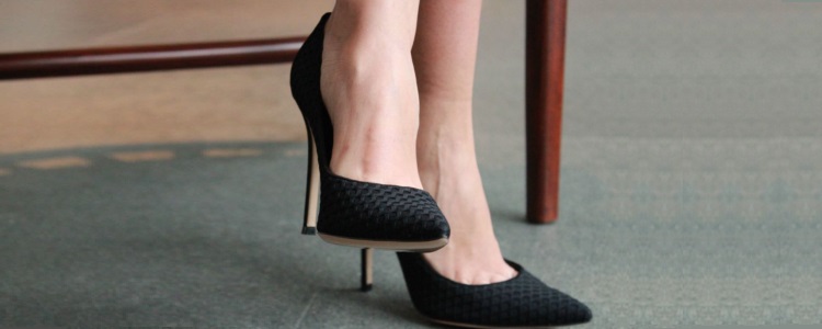 close-up of a woman's feet, probably crossed at the knee -- she wears black fabric heels for work