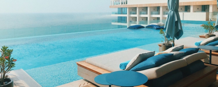 beautiful infinity pool overlooking an ocean, pool loungers are in foreground