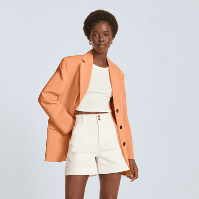 model wears orangey peach boyfriend blazer with flared white shorts and a cropped white tank