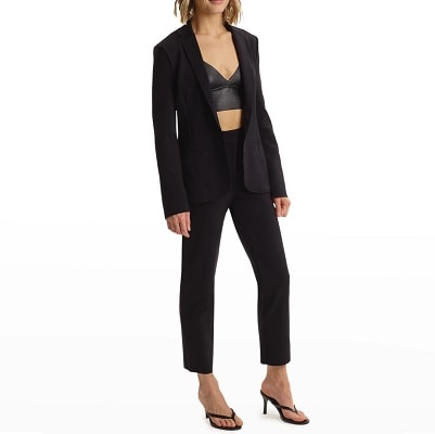 model poses in black suit with cropped trousers; she wears a black leather bralette as a top. (Er... know your office before you do that.) Her shoes are high-heeled thong sandals. 