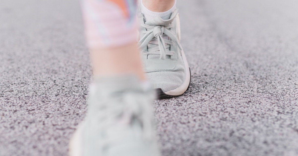 a woman walks on gravel; she wears gray sneakers and a pinkish legging.