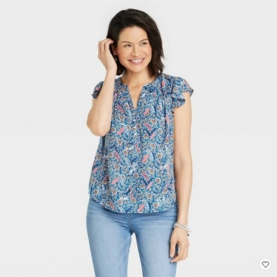 A woman with shoulder-length black hair wearing a blue floral top and light-blue jeans