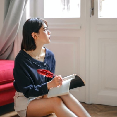 woman writes in journal and looks out window