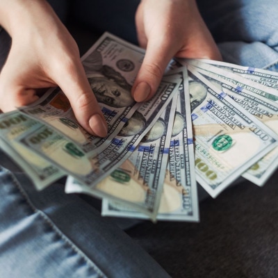 woman with beige nailpolish holding $100 bills and fanning them out