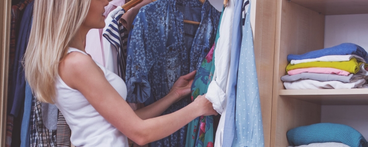 blonde woman looks through her work wardrobe in her closet