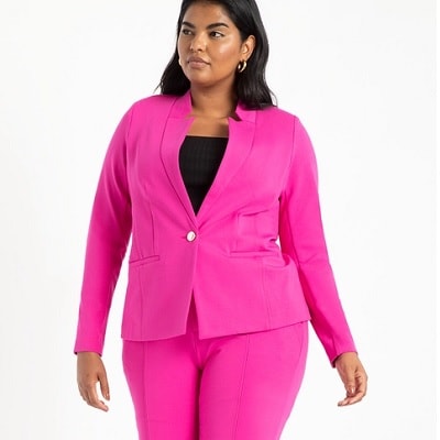A woman with shoulder-length black hair wearing a bright pink blazer, bright pink pants, and a black top