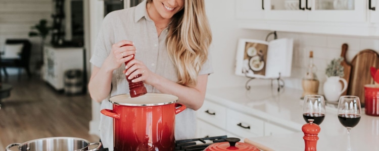 woman cooking fall recipes in kitchen; she is adding salt to a red ombre pot in a mostly white kitchen