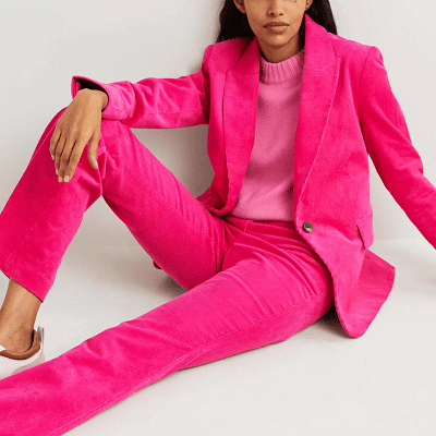 woman sits on ground wearing a hot pink corduroy blazer and hot pink corduroy pants; she has a lighter pink sweater on beneath.