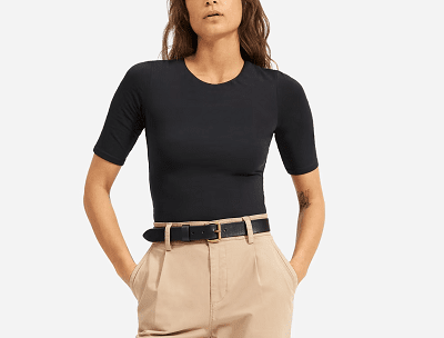 woman wears black crewneck bodysuit with short sleeves and pleated pants with a belt