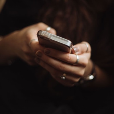 woman wearing rings holds her smart phone in her hand; the background is very dark.