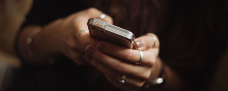 woman wearing rings holds her smart phone in her hand; the background is very dark.
