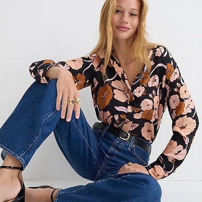 A woman wearing dark blue jeans, black heels, a black belt, and a brown floral blouse