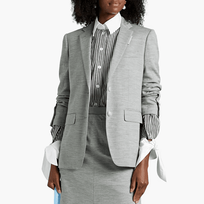 professional young woman wears a gray skirt suit from Burberry - the blazer and skirt are gray melange and she wears a striped blouse beneath it with a sharp collar and weird ties at her wrists instead of cuffs. The jacket is scrunched up so a bit of the stripey shirt is exposed.