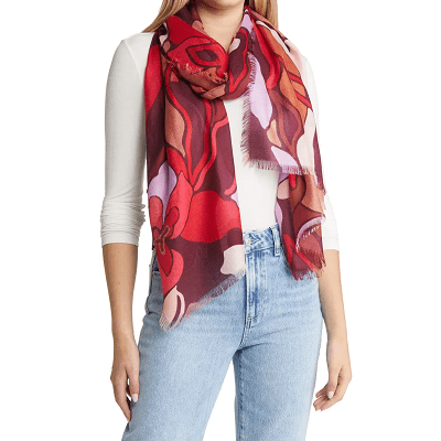 woman models cashmere silk scarf with a burgundy, red, pink, and violet floral pattern; she wears a white layering tee and light blue jeans