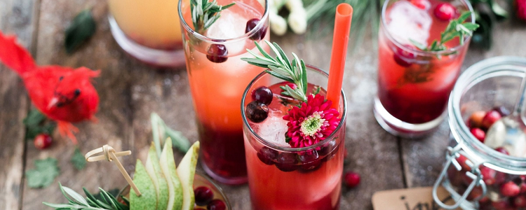 festive holiday drinks are photographed from above; the brown table decorated with green sprigs is visible 