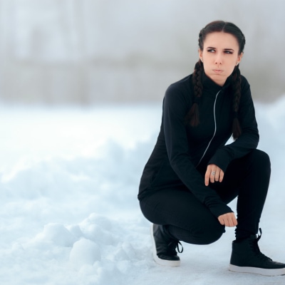 young professional woman takes a break from her run outside in snowy weather; she wears all black