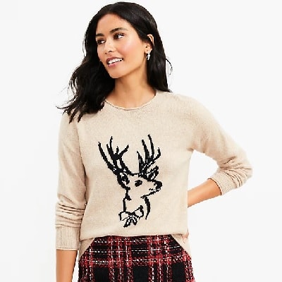 A woman wearing a beige reindeer sweater with a plaid skirt