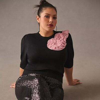 A woman wearing a black sweater with a pink floral applique and sequin pants
