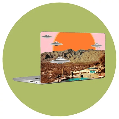 an open laptop (against a graphic backdrop of a greenish circle) has an image on the back of the laptop depicting aliens flying against a pink sky with an orange sun; they are flying over a mountain view with blue waters
