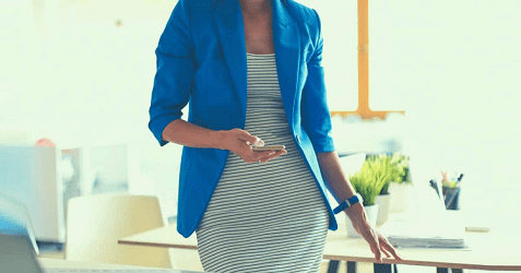 woman wears blue blazer and whiteish dress; she is in an office environment with a lot of beigy white furniture