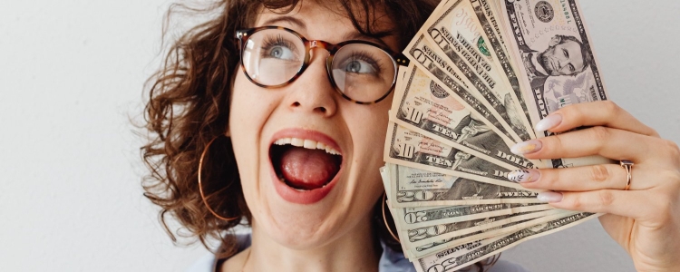 professional young woman with curly hair and glasses looks thrilled to be fanning herself with a stack of cash