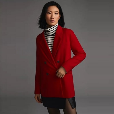 A woman wearing a red blazer, black-and-white striped turtleneck, and black skirt