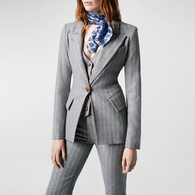 woman wears gray pinstriped pants suit with a matching pinstriped vest instead of a top; she has a blue scarf wrapped around her neck.