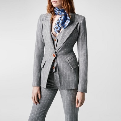 the woman wears a gray pinstripe trouser suit and matching pinstripe vest instead of a top;  she has a blue scarf wrapped around her neck.