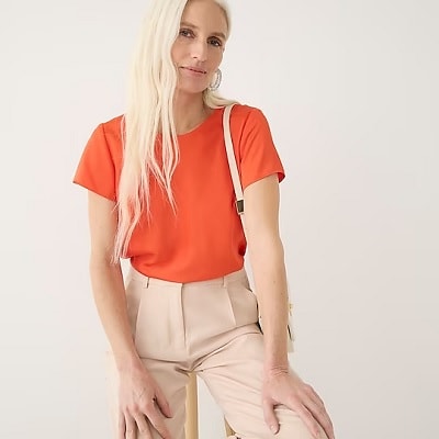 A woman wearing an orange button-back shirt with beige pants and a small beige shoulder bag