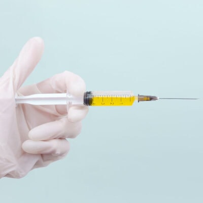 hand covered in white medical glove holds a needle filled with a yellow fluid (presumably, Botox)