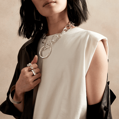 woman wearing silver necklace with large links; she also wears two rings, a white blouse, and apparently a black leather jacket