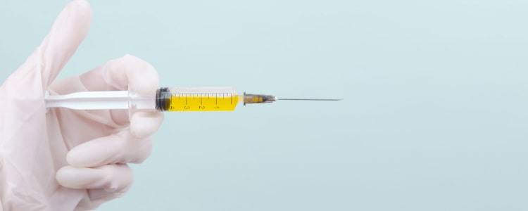 hand covered in white medical glove holds a needle filled with a yellow fluid (presumably, Botox)