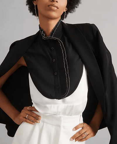 the woman wears a faux collar, aka dickey, under her sweater for a layered workwear -- this dickey is a slightly sheer black and white option with a high, almost Mandarin-like neckline